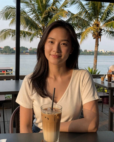 Laotian woman enjoying iced coffee at a Mekong riverside cafe in Vientiane - modern Laotian dating lifestyle